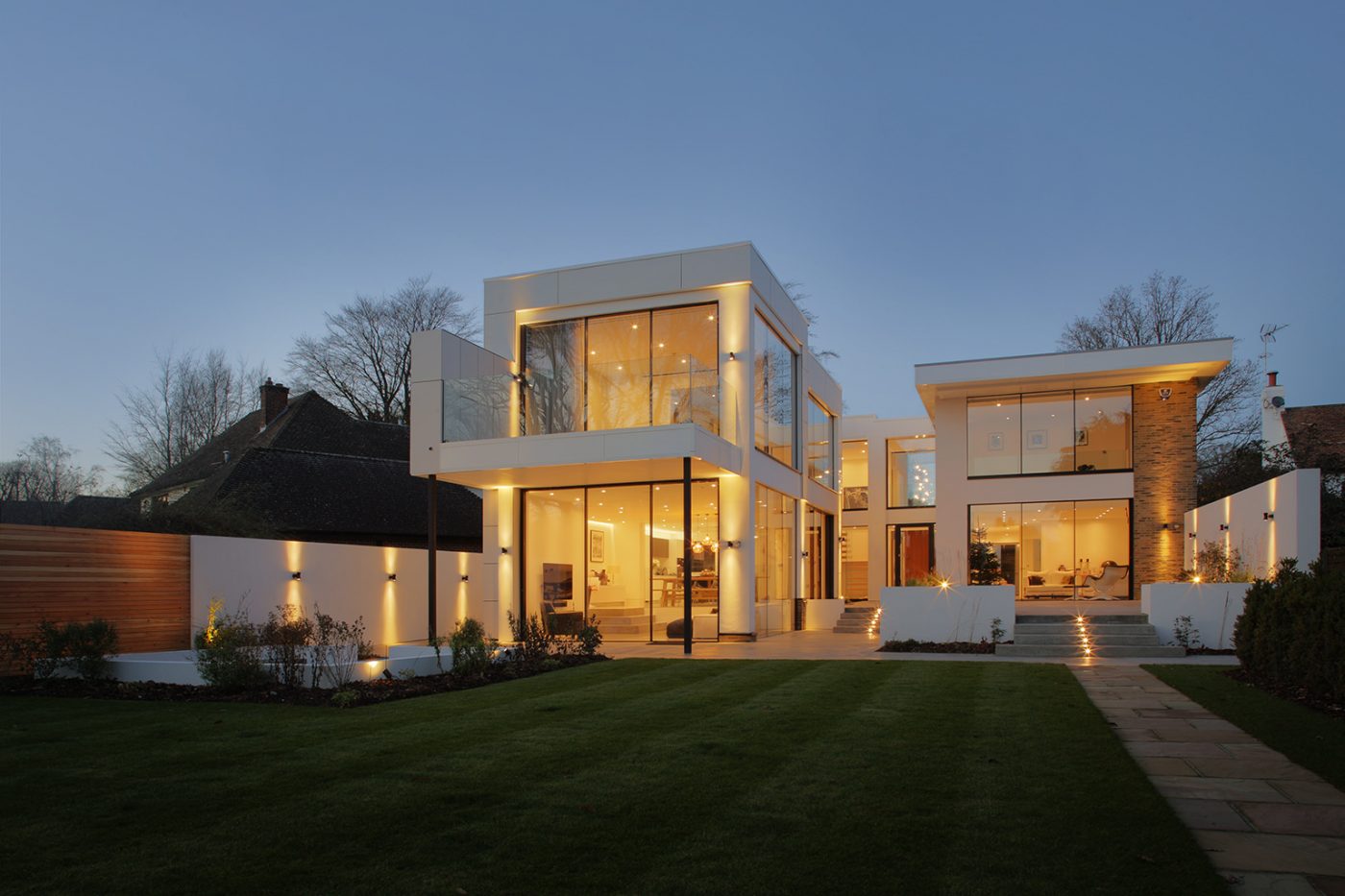 Contemporary white house at dusk with full-height glazing and lit garden